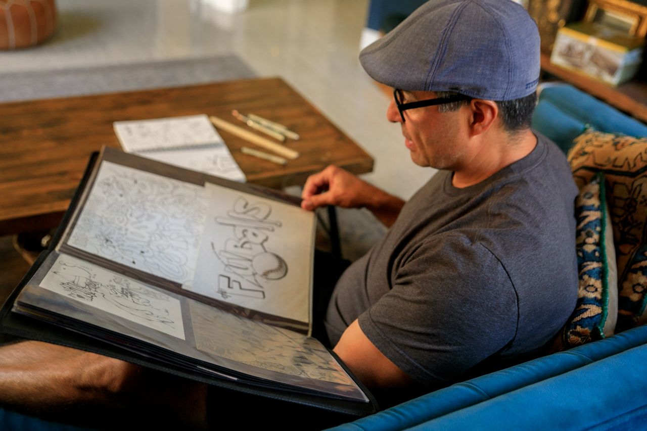 Services A man sits on a sofa reviewing his art portfolio filled with various illustrations.