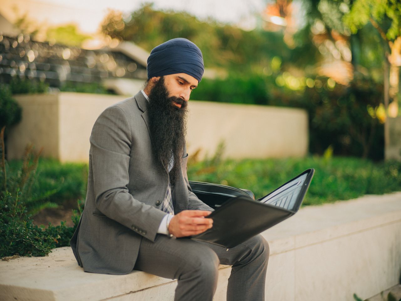 Services A business professional in a turban reading a document while sitting outside in a formal suit.